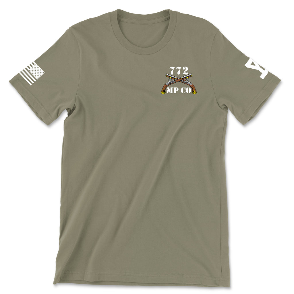 Front view of a coyote brown t-shirt for the 772nd Military Police Company. The left chest features a white graphic with the number '772' above a blue infantry disc and crossed flintlock pistols, with 'MP CO' written at the bottom. A white American flag patch is displayed on the right sleeve
