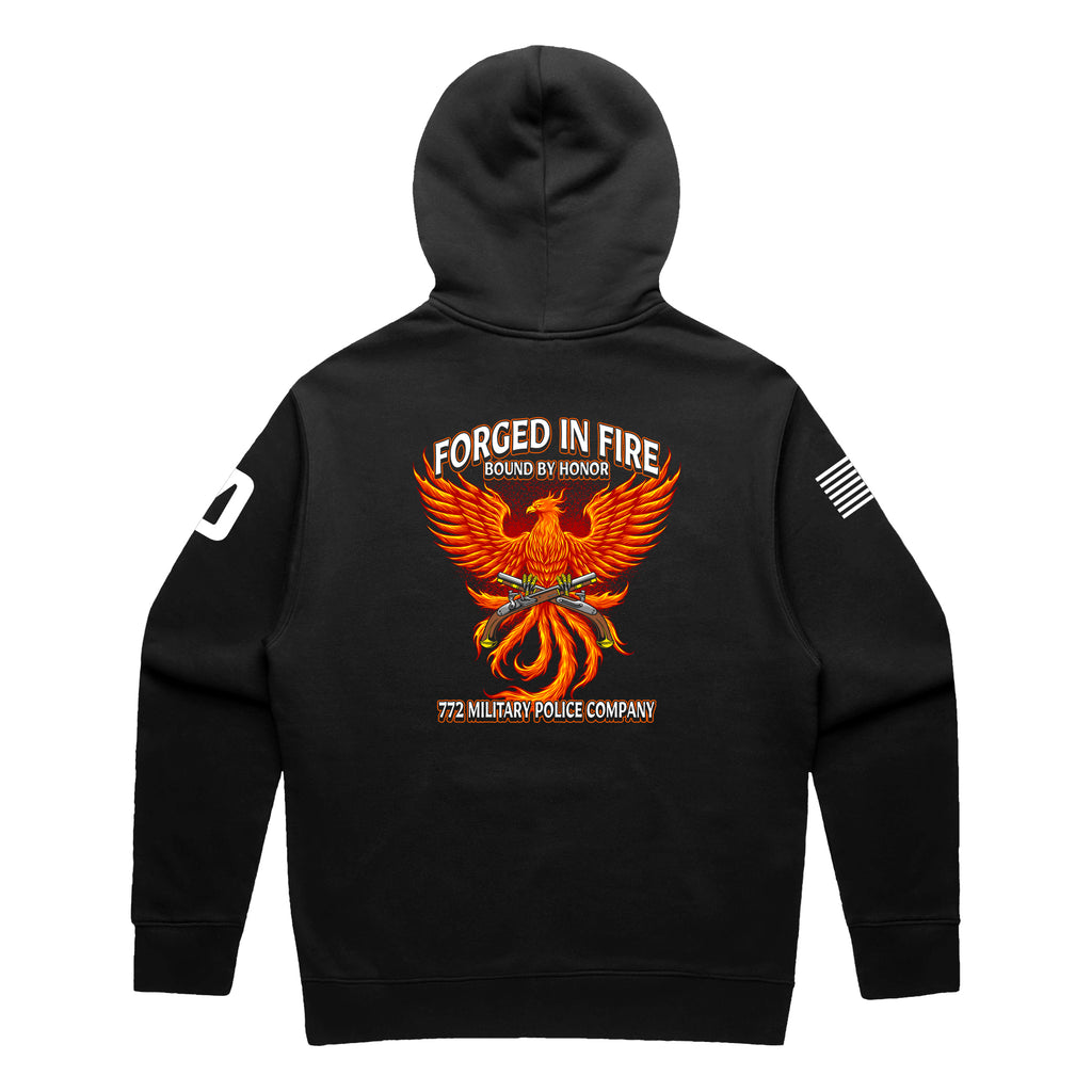 Back view of a black pullover hoodie for the 772nd Military Police Company. The design features a large orange and yellow phoenix rising from flames, with crossed flintlock pistols and a blue infantry disc at its center. Banners above read 'FORGED IN FIRE' and 'BOUND BY HONOR,' with '772 MILITARY POLICE COMPANY' written in red at the bottom. A white American flag patch is on the right sleeve.