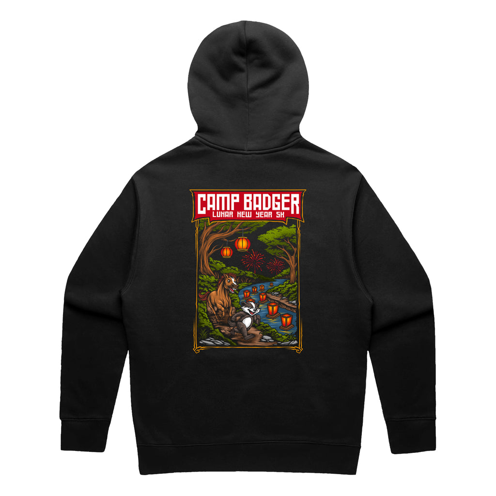 Back view of a black pullover hoodie for the Camp Badger Lunar New Year 5K. The large rectangular graphic features a festive night scene with a badger and a horse standing by a river lit by glowing red lanterns. The text 'CAMP BADGER' is displayed in bold at the top, followed by 'LUNAR NEW YEAR 5K' against a background of a forest, a bridge, and fireworks in the sky.