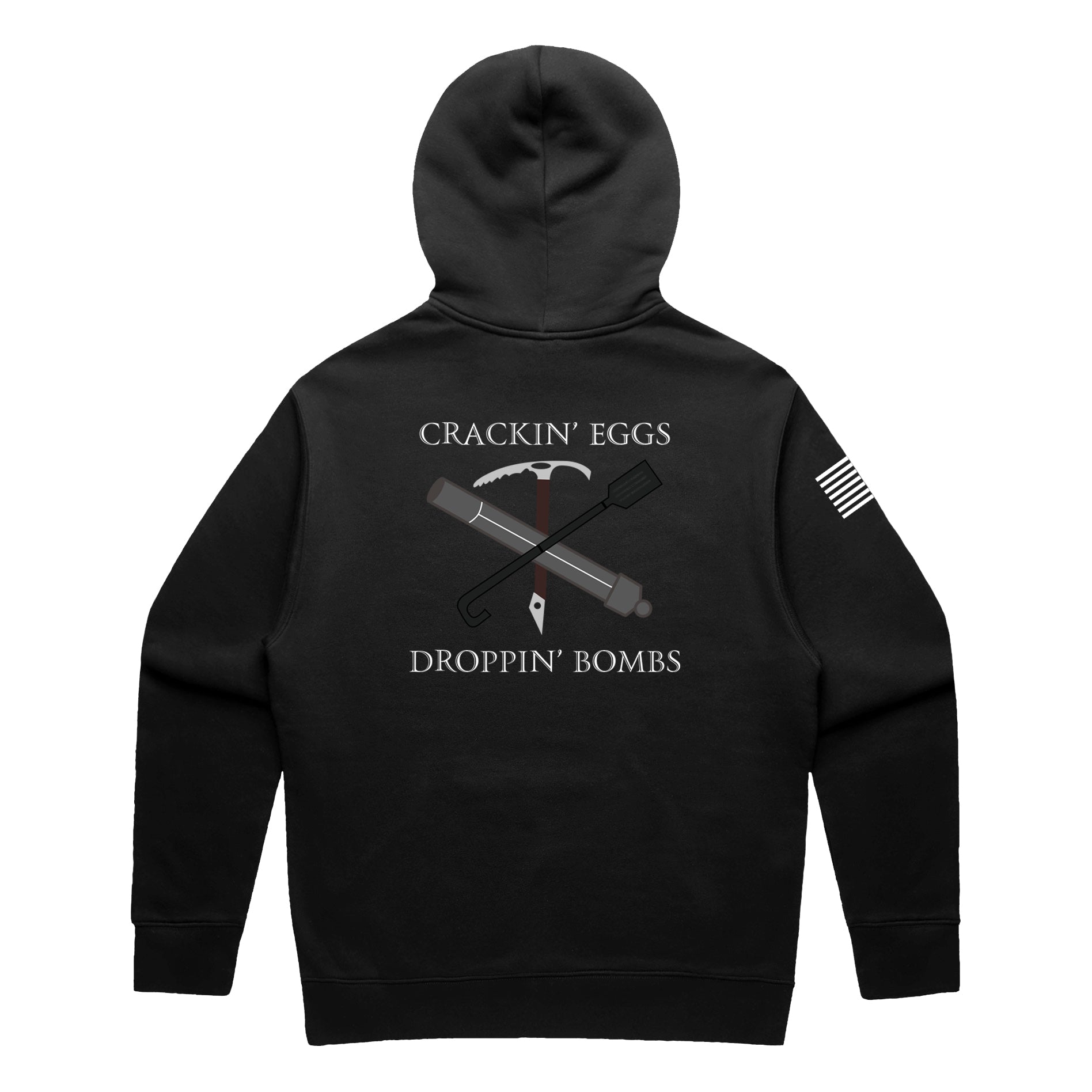 Back view of a black pullover hoodie featuring the text 'CRACKIN’ EGGS' at the top and 'DROPPIN’ BOMBS' at the bottom in white serif font. The central graphic shows a crossed ice axe and a tactical breaching tool (Halligan bar) with a small white diamond-shaped tag hanging from the center. A white American flag patch is visible on the right sleeve.