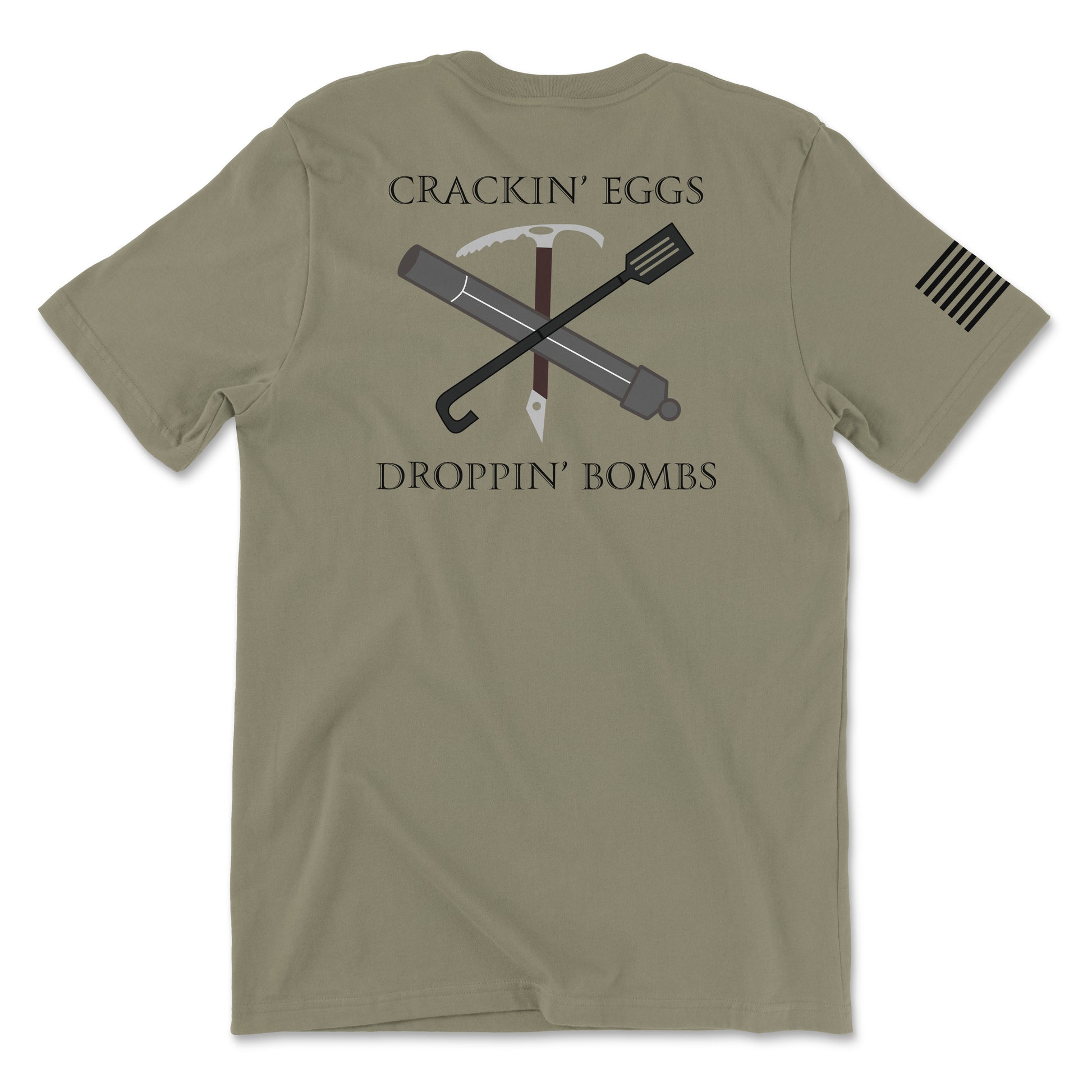 Back view of a coyote brown t-shirt featuring the text 'CRACKIN’ EGGS' at the top and 'DROPPIN’ BOMBS' at the bottom in white serif font. The central graphic shows a crossed ice axe and a tactical breaching tool (Halligan bar) with a small white diamond-shaped tag hanging from the center. A white American flag patch is visible on the right sleeve.