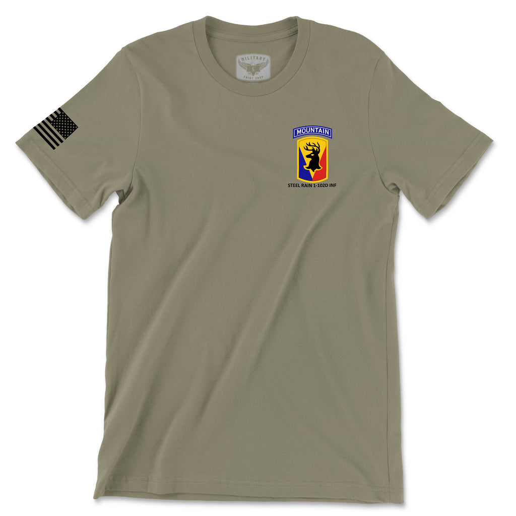 Front view of a coyote brown t-shirt for the 1st Battalion, 102nd Infantry Regiment (1-102D INF). The left chest features a yellow unit crest with a red stag silhouette and a 'MOUNTAIN' tab above it. The text 'STEEL RAIN 1-102D INF' is printed below the insignia. A black American flag patch is displayed on the right sleeve.