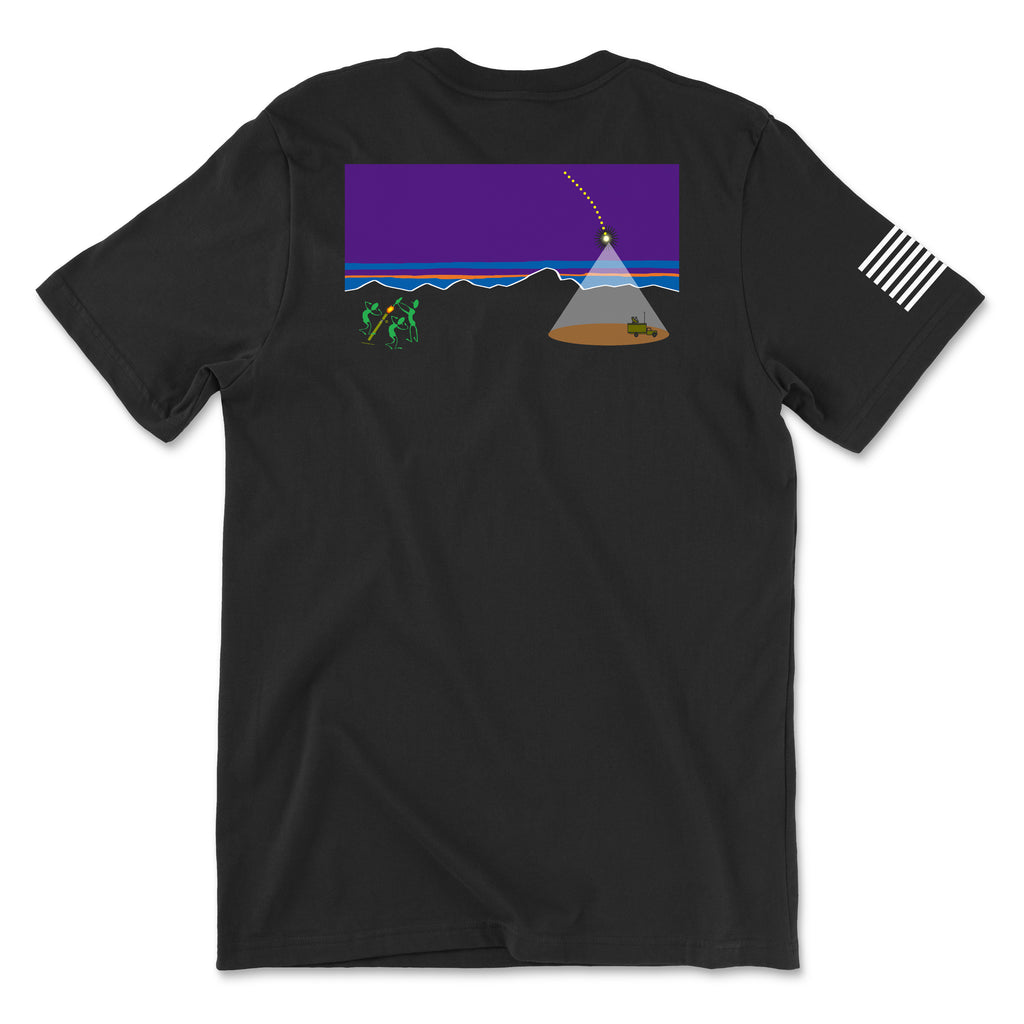 Back view of a black t-shirt featuring a rectangular graphic parodying the Patagonia logo. The design shows a purple night sky over mountain silhouettes with a dotted line representing a mortar trajectory arc between a vehicle and a group of soldiers. A white American flag patch is visible on the right sleeve.